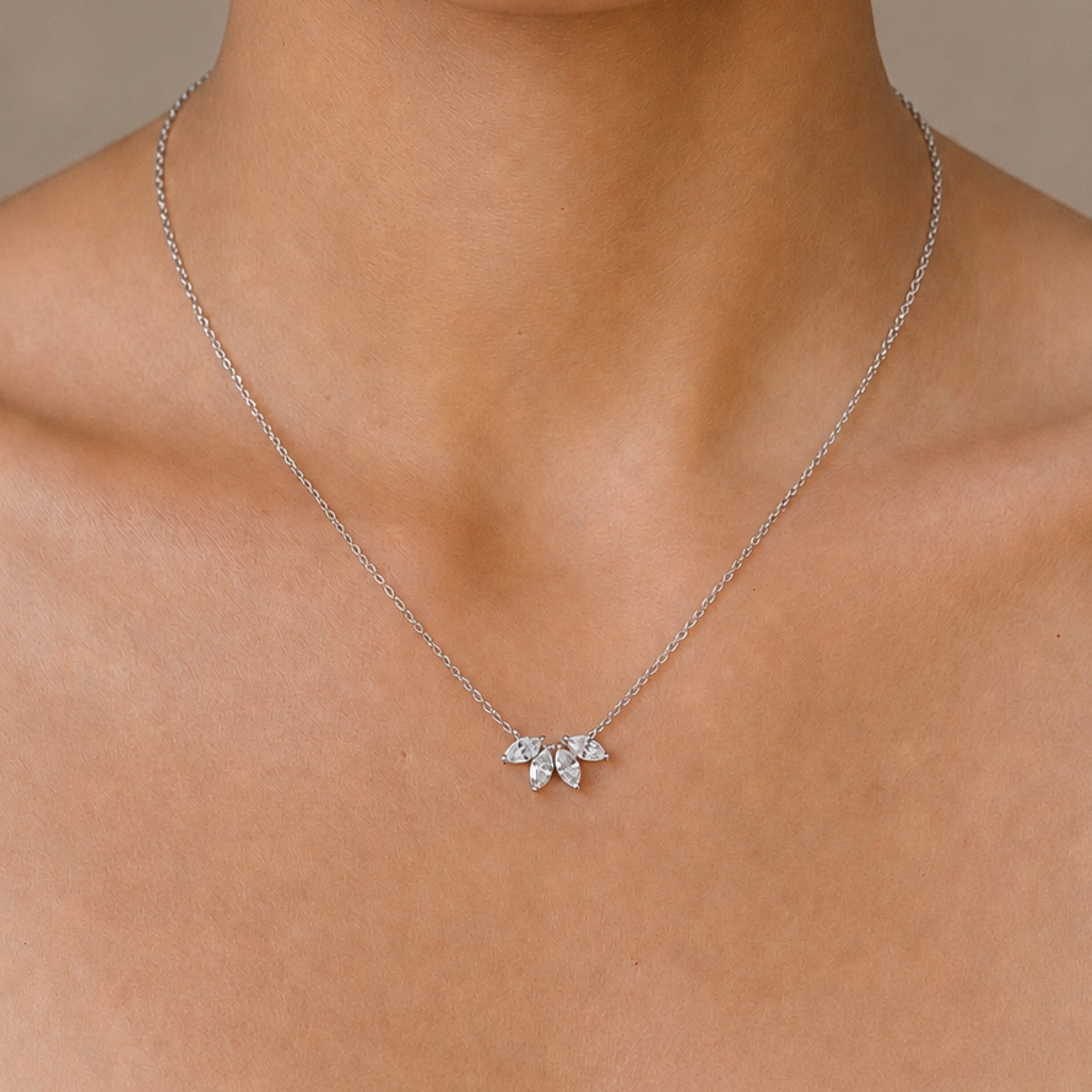 A delicate silver chain necklace with a small flower-shaped pendant set with clear stones, shown worn on a model's neck.