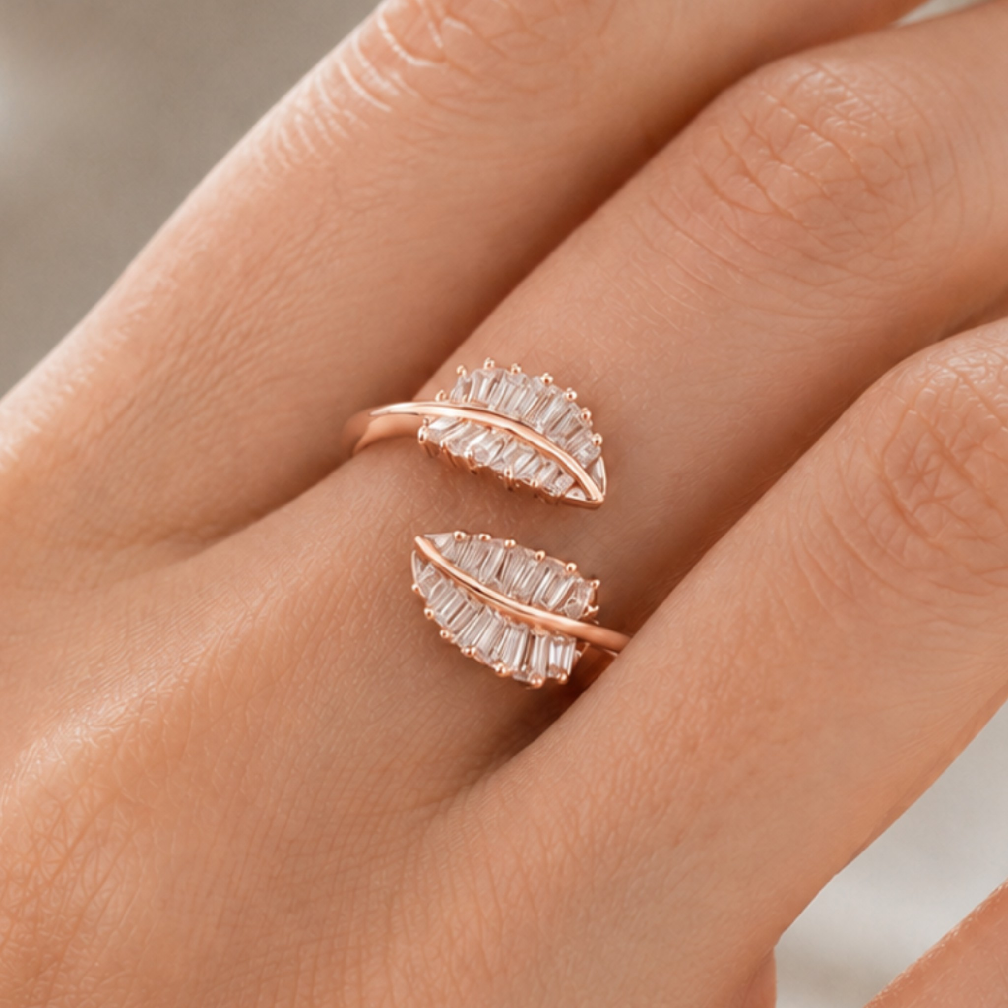 A close-up of a hand wearing a rose gold ring with two leaf-shaped settings set with clear baguette crystals.