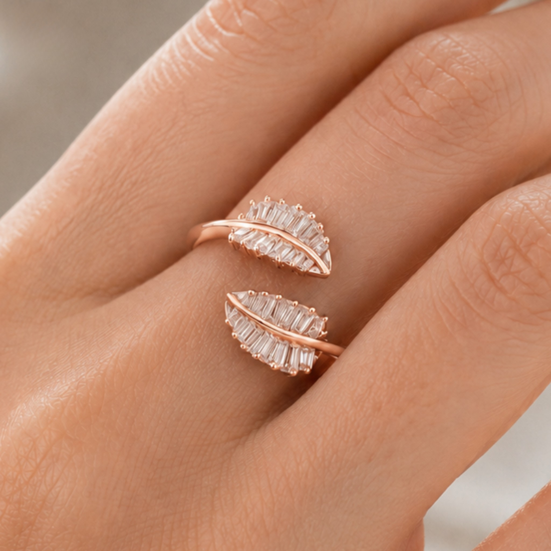 A close-up of a hand wearing a rose gold ring with two leaf-shaped settings set with clear baguette crystals.