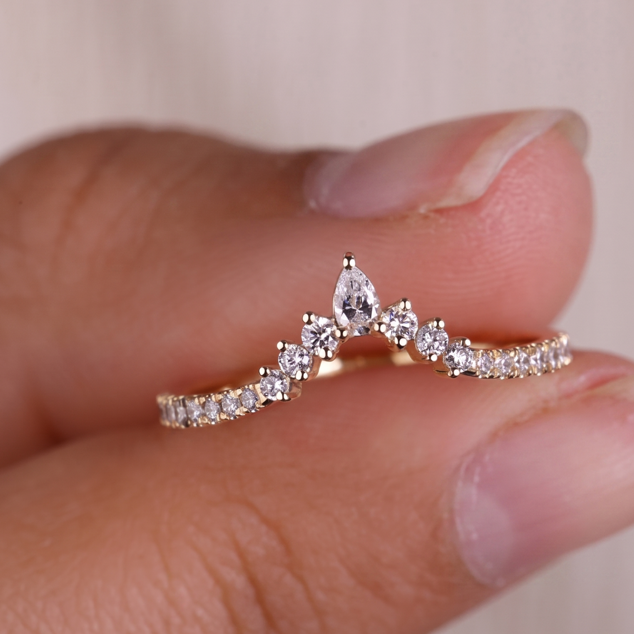 A delicate gold ring with a row of clear stones and a central pear-cut gemstone, shown worn on a person's fingers.