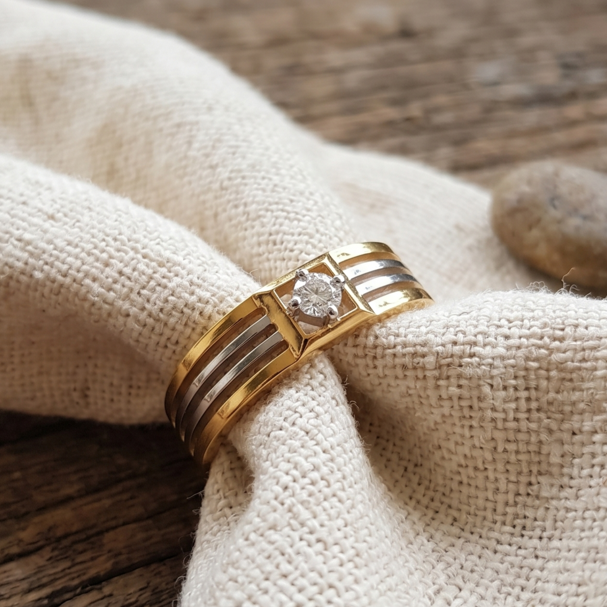 A gold ring with a round clear gemstone and three parallel channel settings, displayed on a textured beige fabric napkin over a rustic wooden surface.