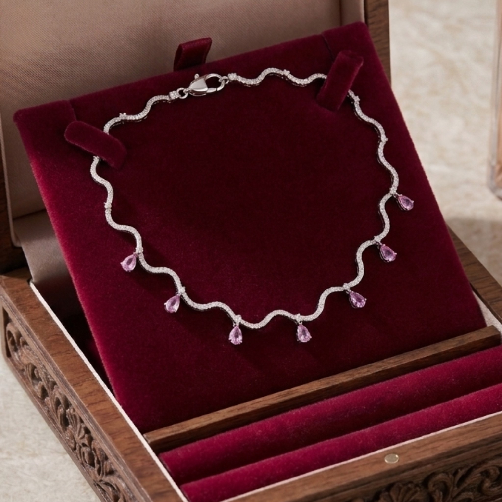 A silver wavy chain necklace with five dangling light purple crystal drops, displayed on a deep red velvet jewelry stand inside a carved wooden box.