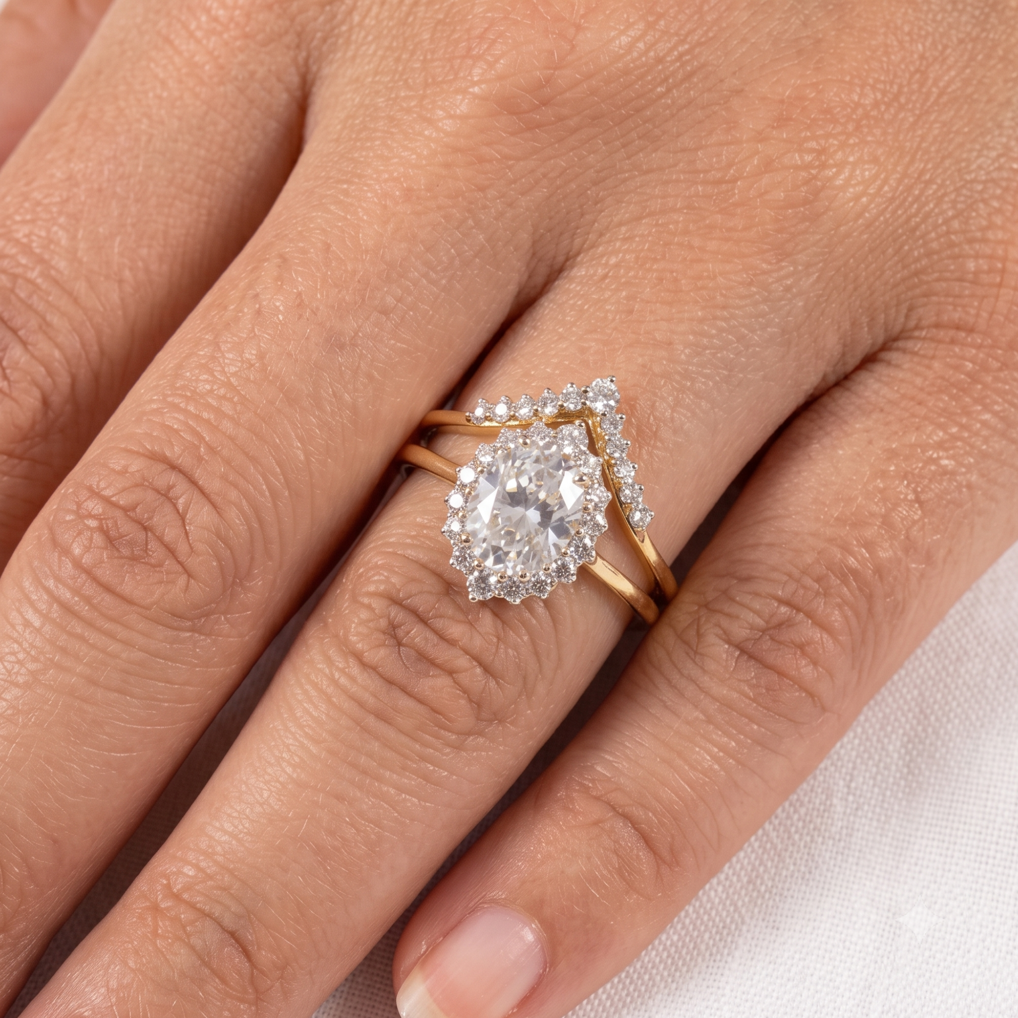 A close-up of a hand wearing a gold ring set with a large pear-cut clear gemstone and smaller surrounding stones, with a matching slim gold band visible behind it.