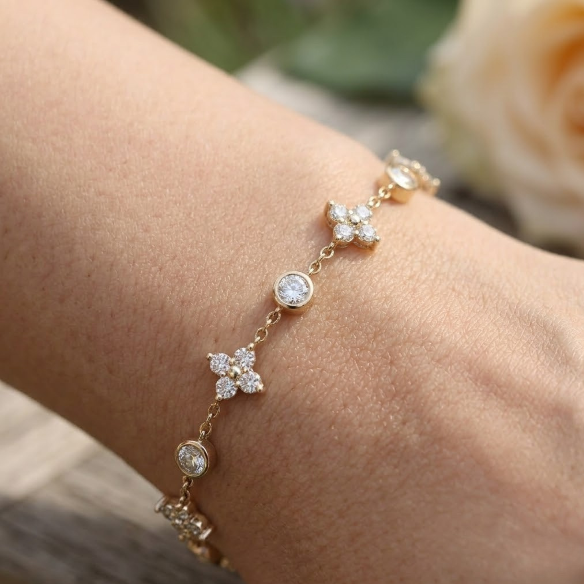 A delicate gold chain bracelet with floral and round-cut crystal motifs, shown worn on a person's wrist against a softly blurred background.