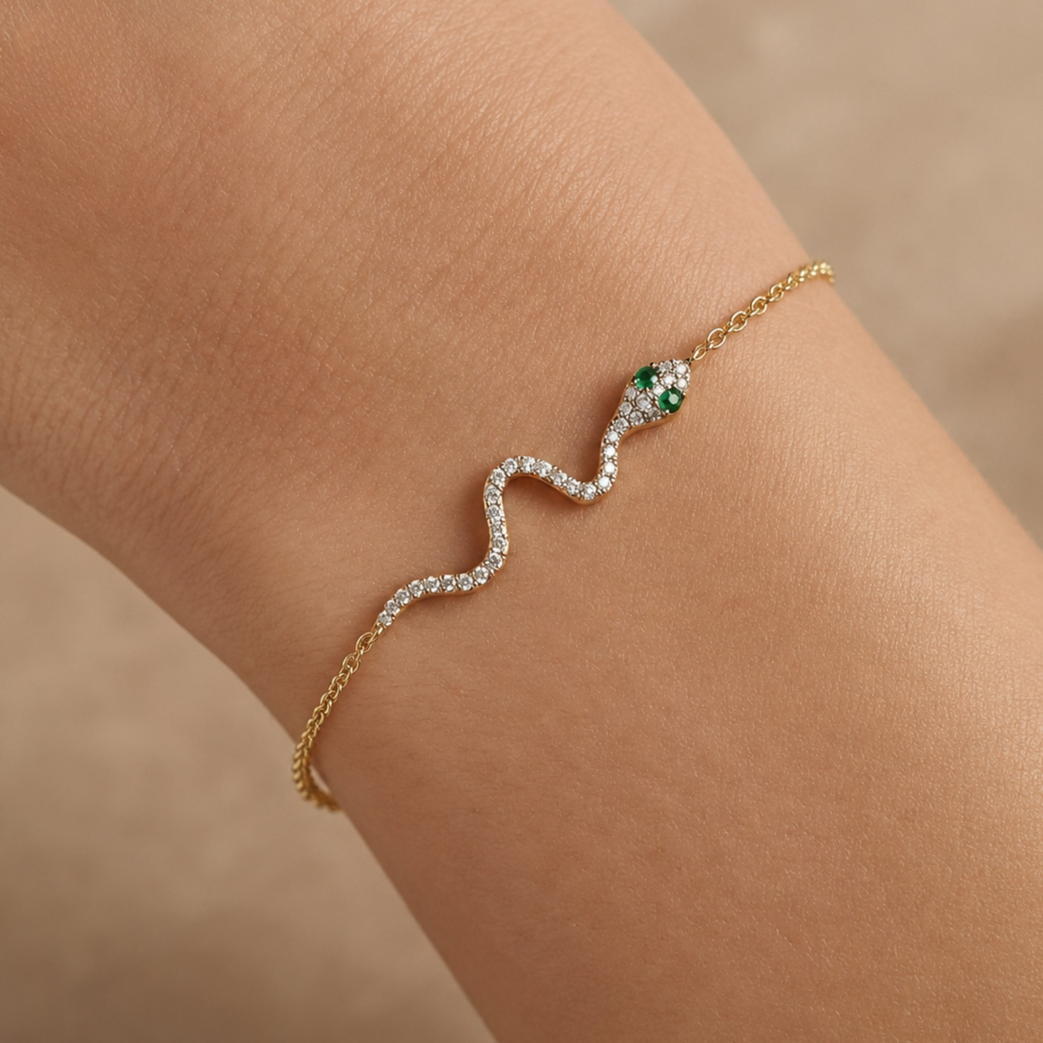 A delicate gold chain bracelet worn on a wrist, featuring a wavy silver pavé section with clear stones and a green and gold snake head at the end.