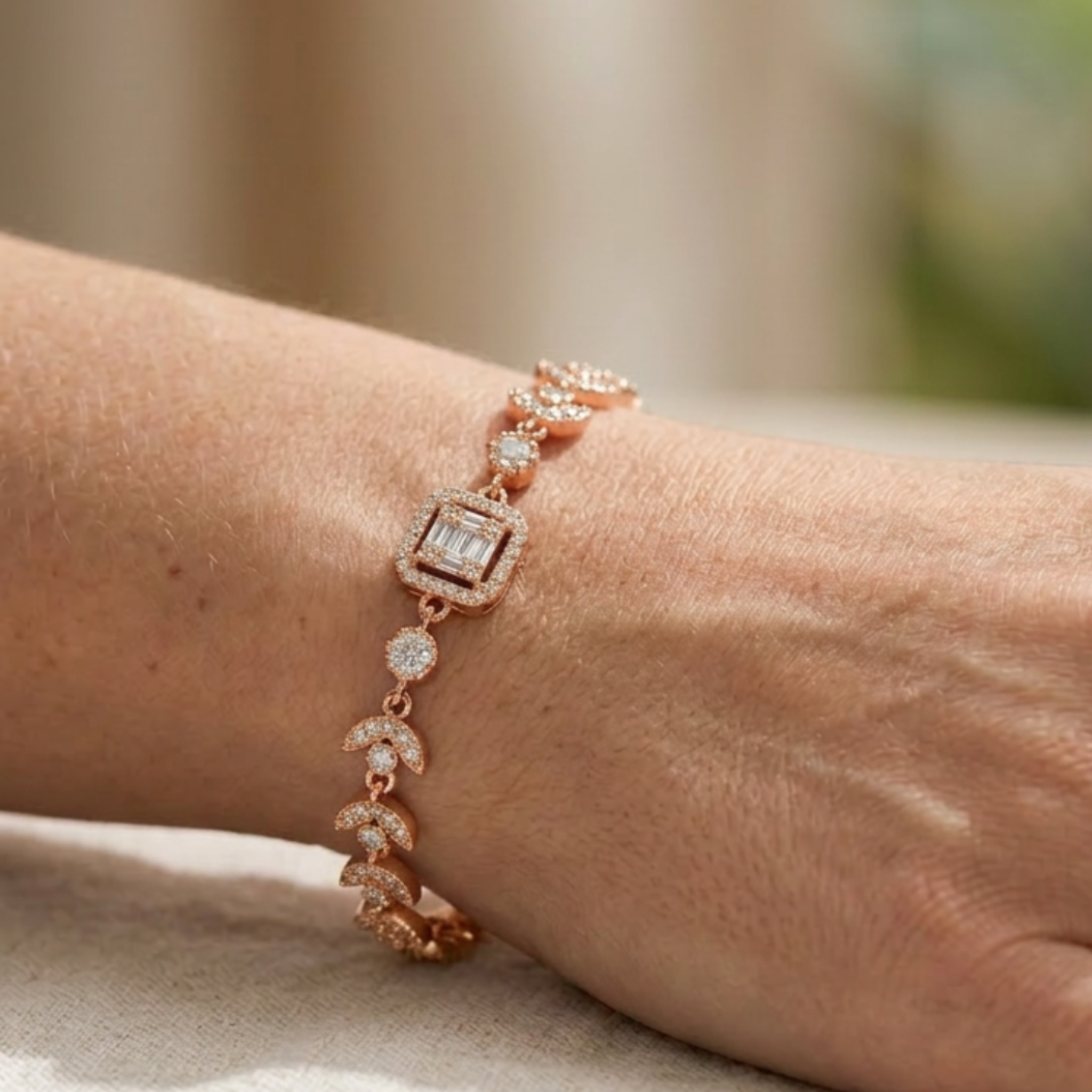 A rose gold bracelet with diamond accents, featuring a square bezel-set diamond and crescent moon links, shown worn on a wrist.