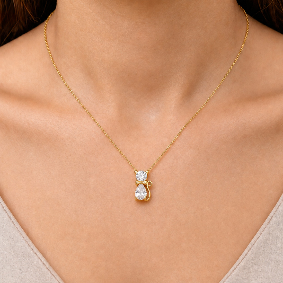 A gold necklace with a pendant shaped like a small cat holding a teardrop-shaped clear gemstone, shown worn on a model's neck.