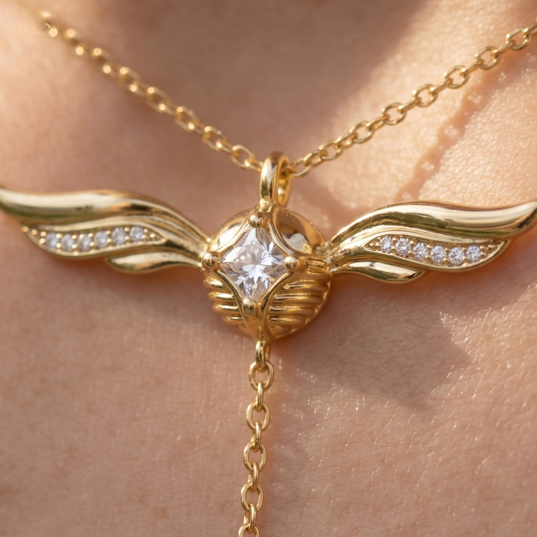 Gold wing pendant necklace with a clear central gemstone and small clear stones along the wings, shown worn on skin.