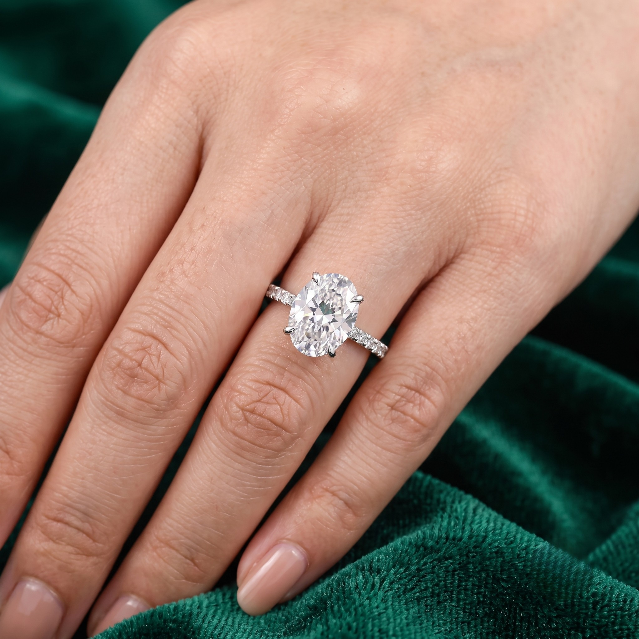 A close-up of a hand wearing a silver-toned ring with a large oval-cut clear gemstone, set against a dark green velvet fabric background.