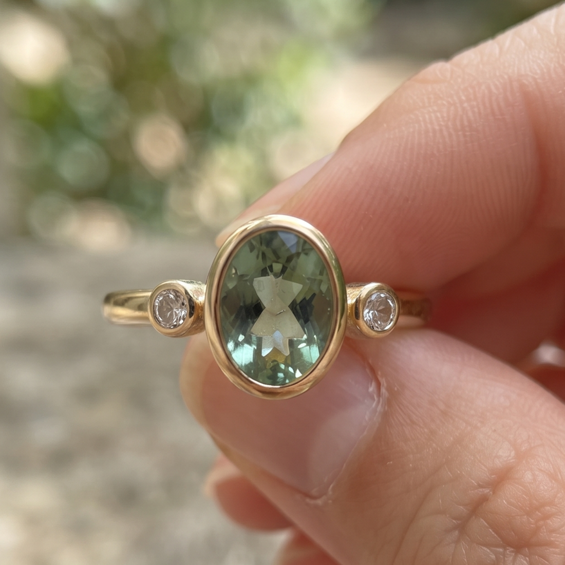 Front view of a 2 CT oval green gemstone three-stone bezel ring in yellow gold.