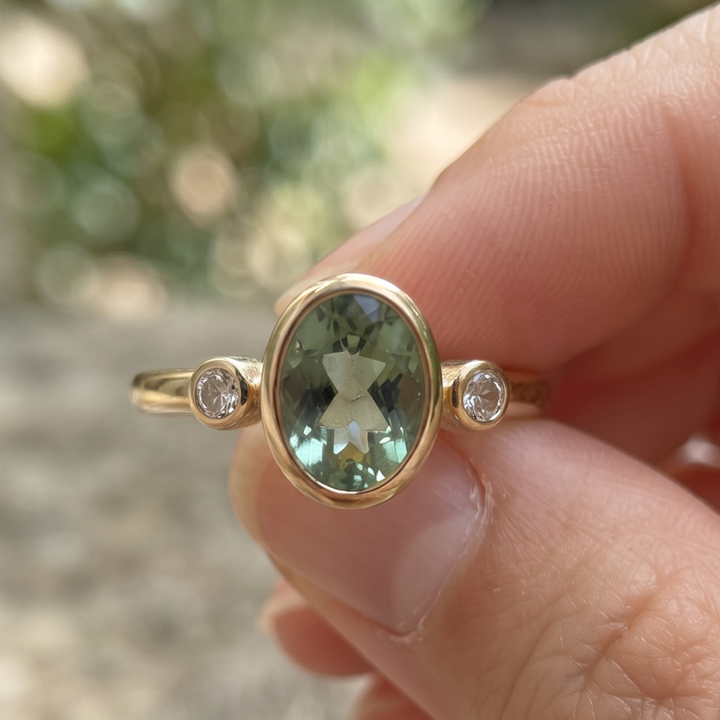 Front view of a 2 CT oval green gemstone three-stone bezel ring in yellow gold.