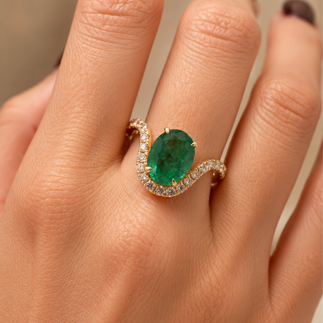 A close-up of a hand wearing a yellow gold ring with a large oval green emerald center stone and a curved pavé setting of small clear stones.
