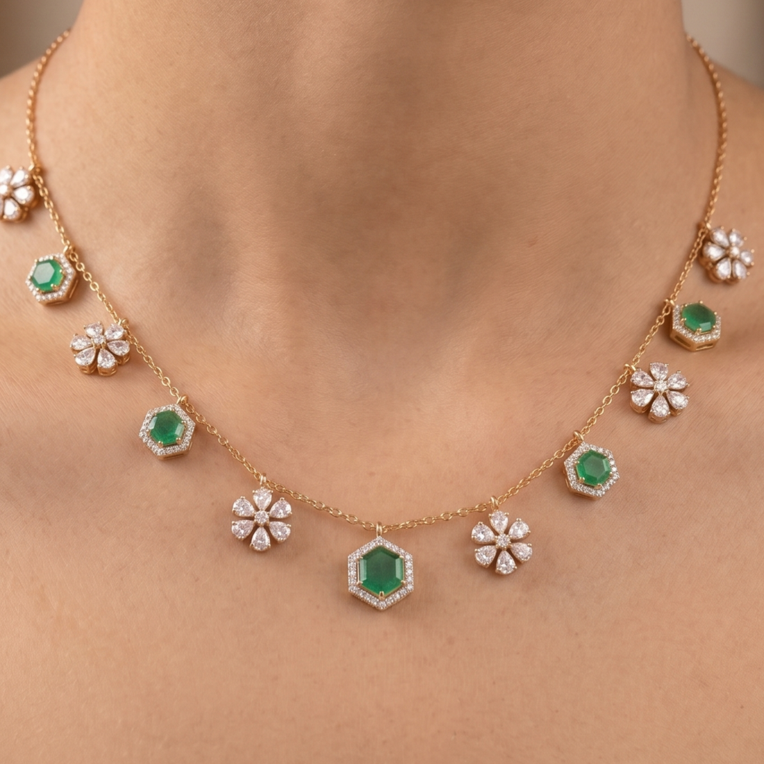 A gold necklace with emerald-cut green gemstones and diamond-like floral accents, shown worn on a model's neck.
