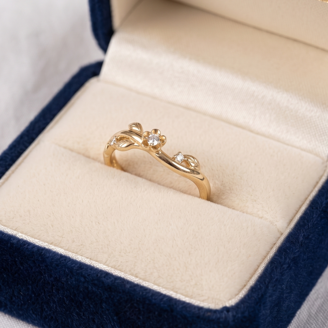 A delicate gold ring with a small central clear gemstone and smaller side stones, displayed in an open navy blue velvet ring box with a cream satin interior.