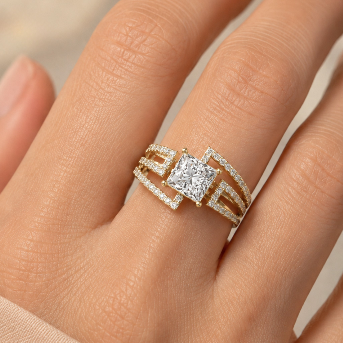 A close-up of a hand wearing a geometric yellow gold ring with a princess-cut diamond center stone and pavé-set side details.