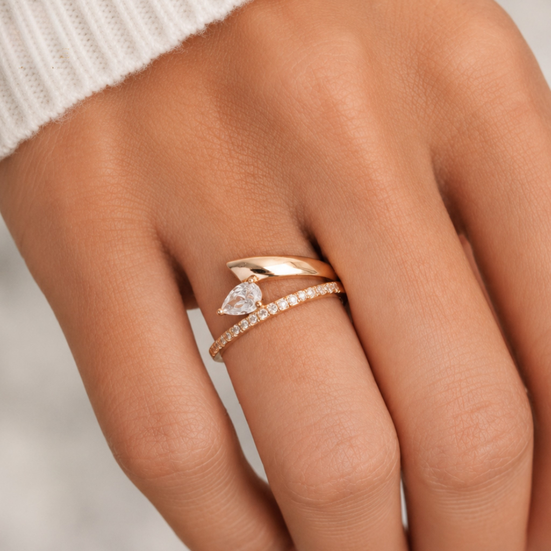 A close-up of a hand wearing a rose gold ring set with a marquise-cut clear gemstone and a thin pavé band.