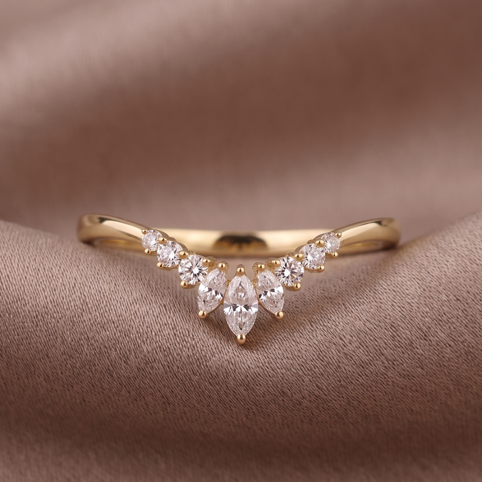A gold V-shaped ring with marquise and round-cut clear stones, displayed on a draped brown fabric background.