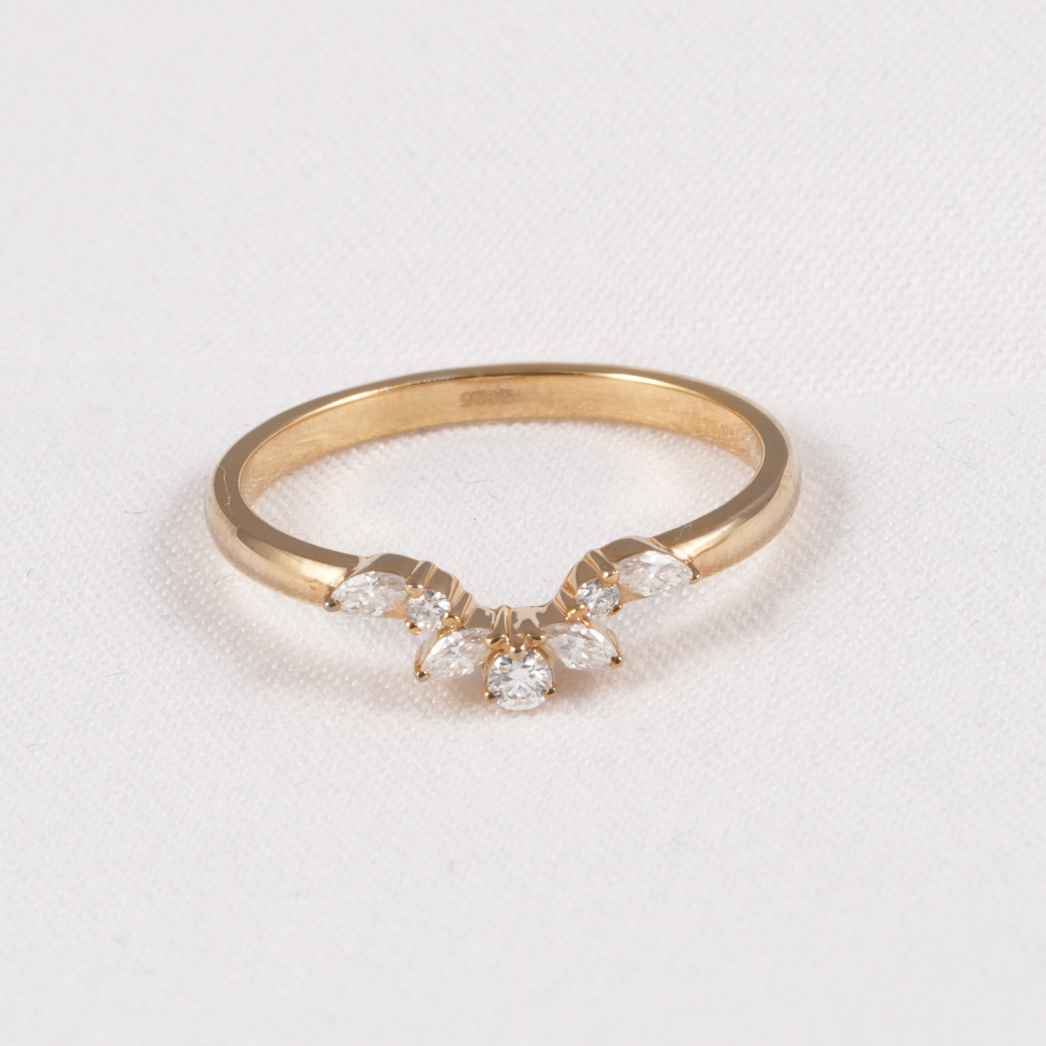 A yellow gold ring featuring a small floral cluster with marquise-cut and round clear gemstones, displayed on a textured white background.