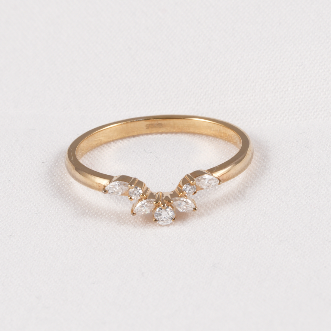 A yellow gold ring featuring a small floral cluster with marquise-cut and round clear gemstones, displayed on a textured white background.