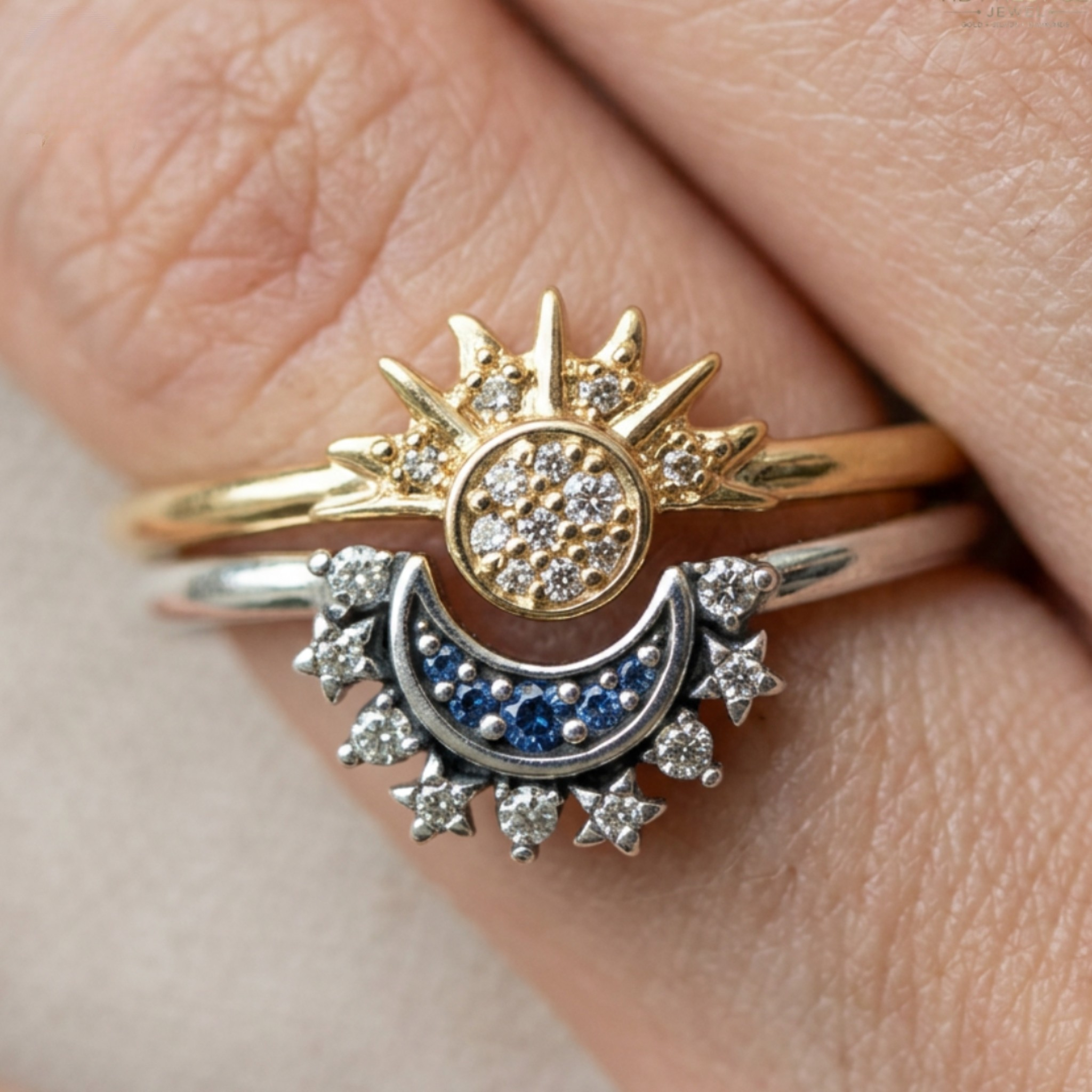 A close-up of a hand wearing a two-tone ring set featuring a gold sunburst with small clear stones and a silver crescent moon with blue and clear stones.