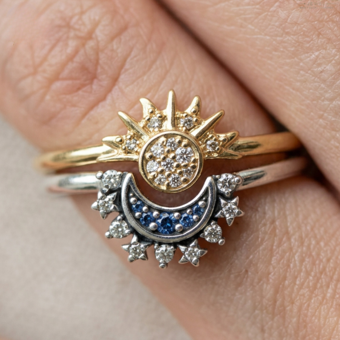 A close-up of a hand wearing a two-tone ring set featuring a gold sunburst with small clear stones and a silver crescent moon with blue and clear stones.