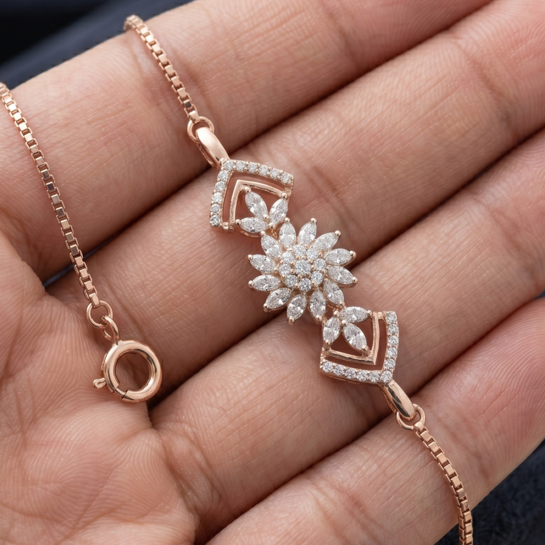 A rose gold bracelet with a central flower motif and diamond-like clear stones, displayed on a person's hand.