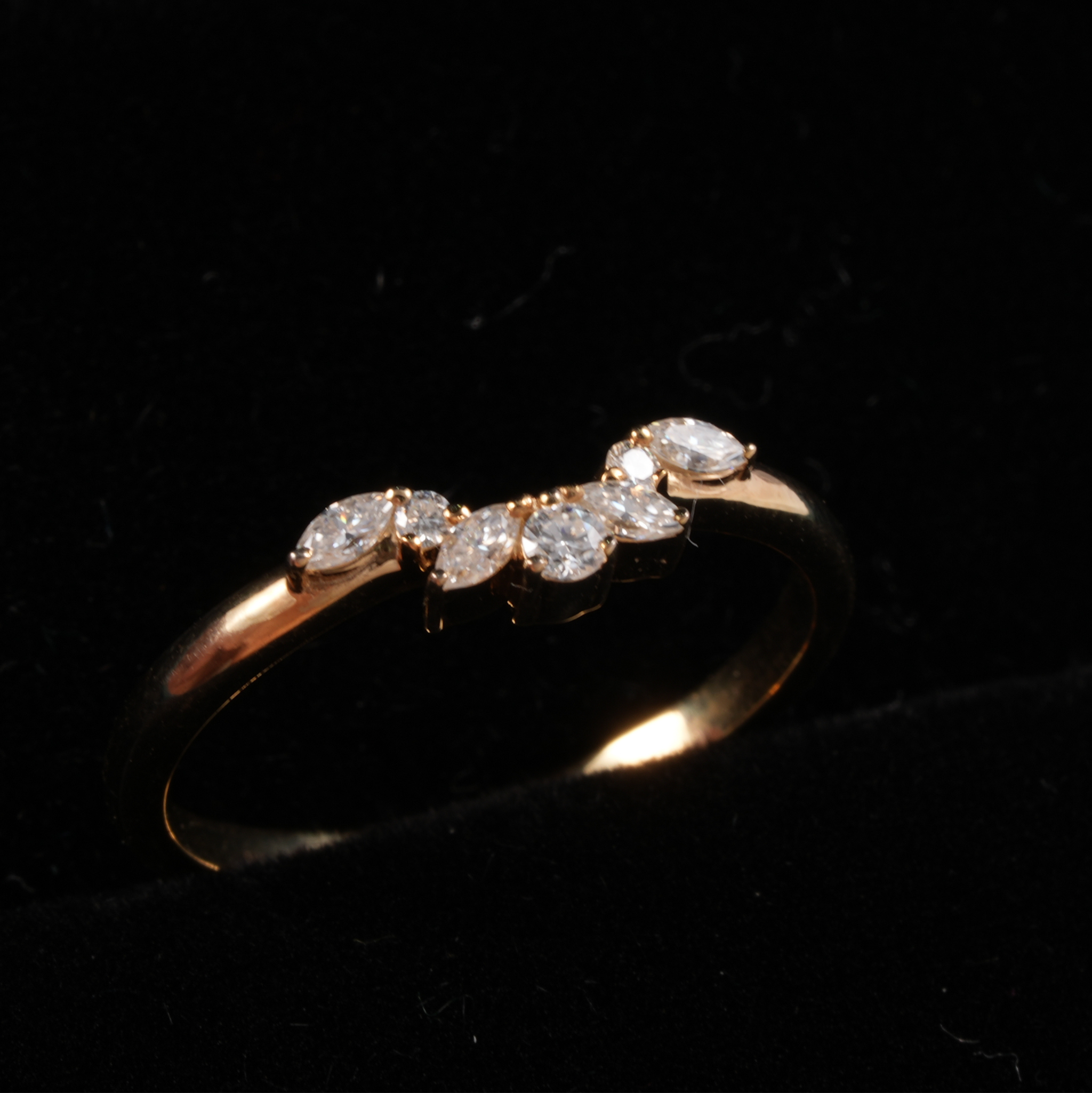 A rose gold ring with a curved row of clear marquise and round-cut gemstones, displayed on a black background.