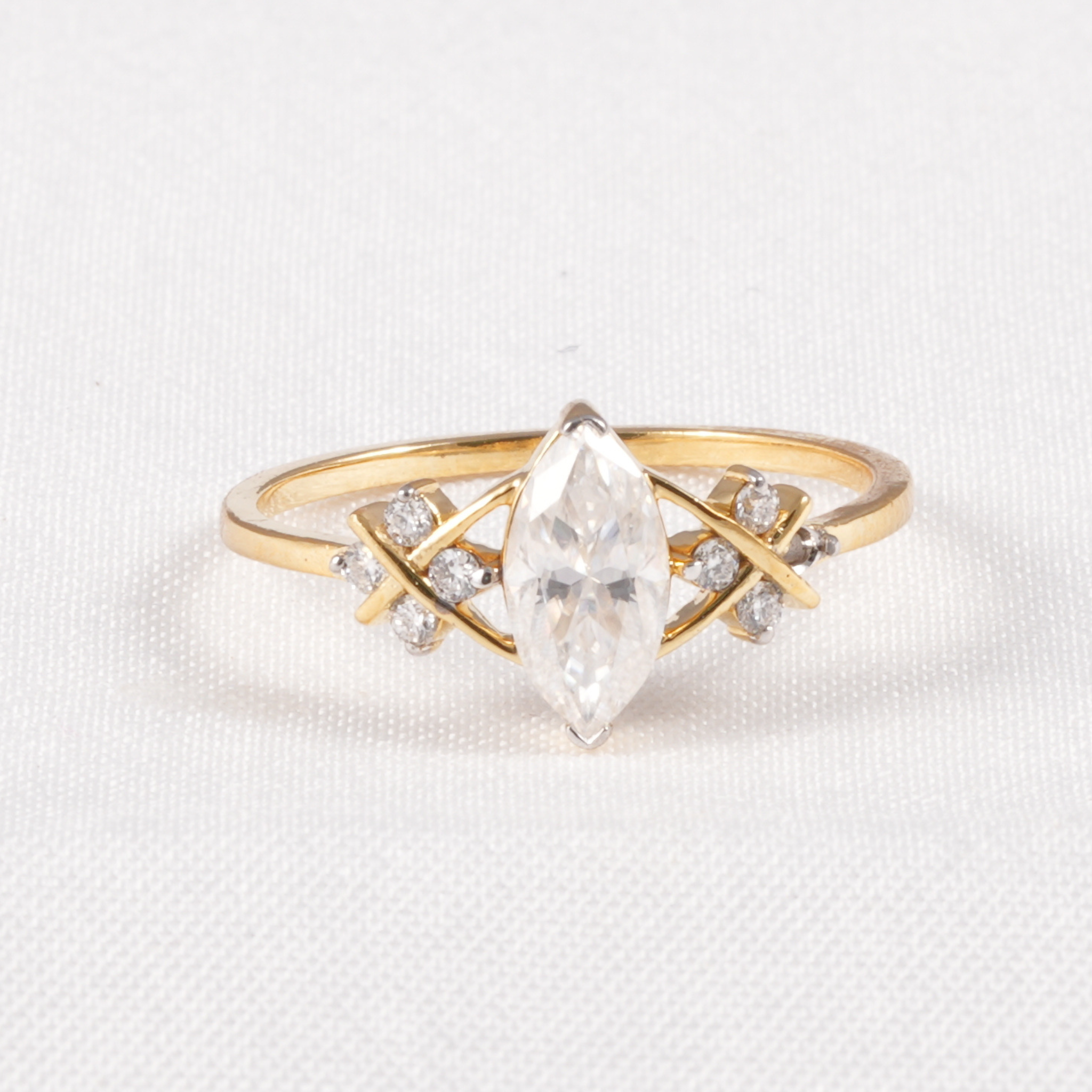 A yellow gold ring featuring a marquise-cut clear center stone and small clear accent stones set in an open geometric design, photographed on a textured white background.