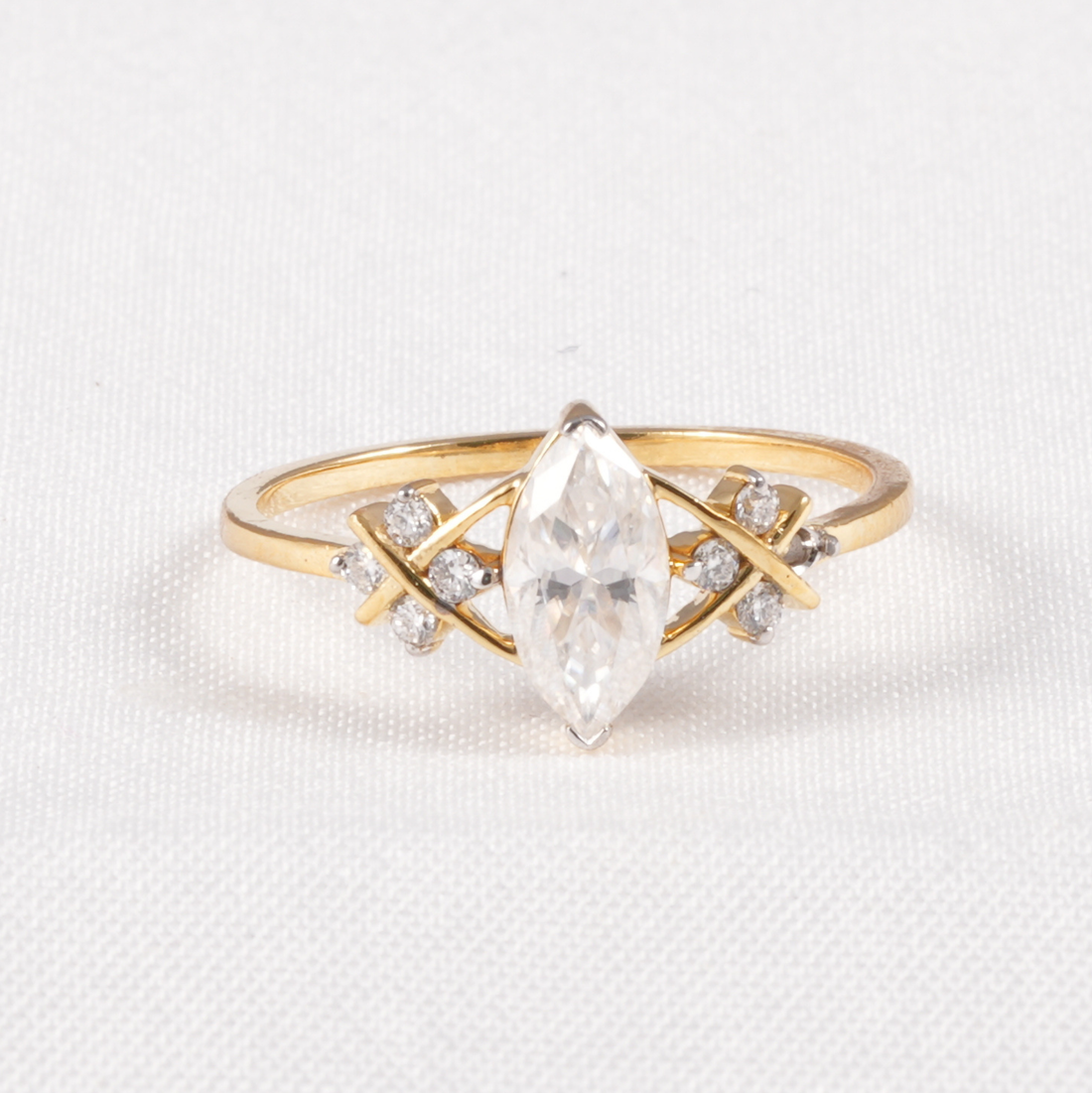 A yellow gold ring featuring a marquise-cut clear center stone and small clear accent stones set in an open geometric design, photographed on a textured white background.