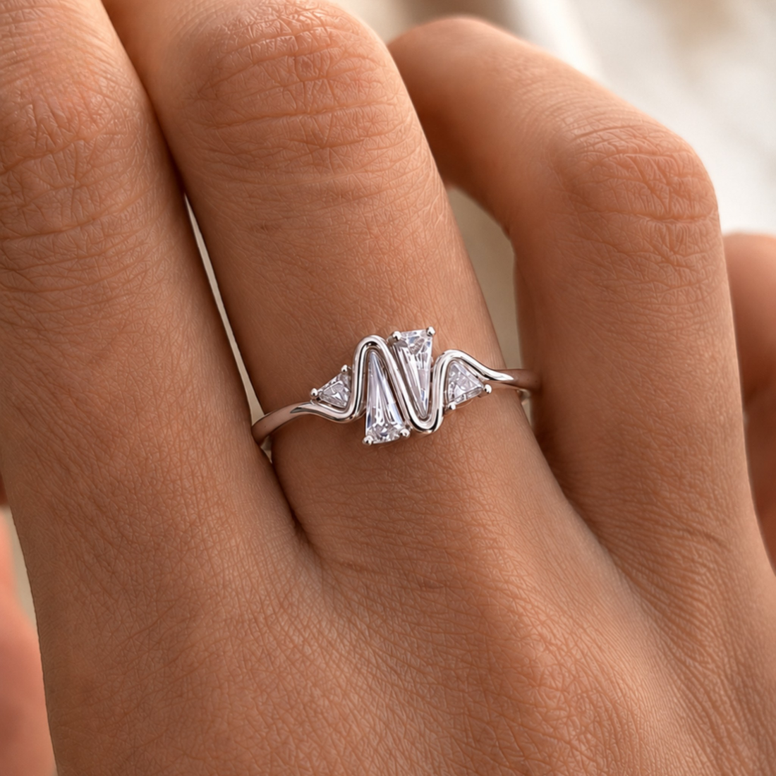 A silver ring with a wavy, zigzag-cut center stone and small marquise-cut side stones, shown worn on a hand.
