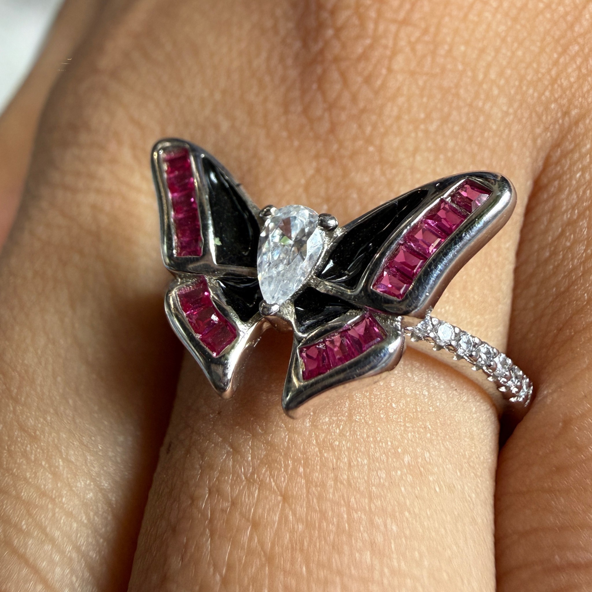A silver butterfly ring with black enamel and bright pink gemstone accents, worn on a finger.