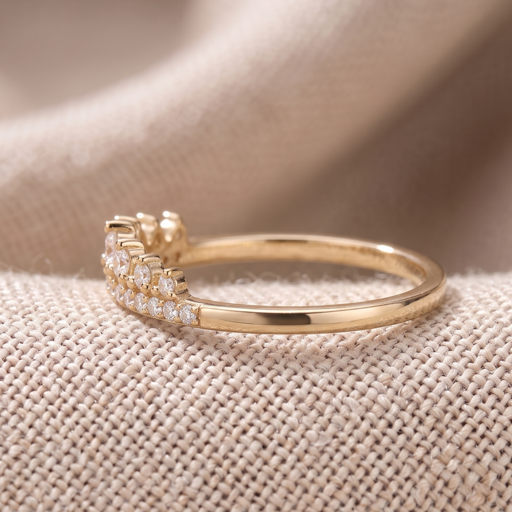 A gold ring with a pavé diamond band and a small diamond accent on the opposite side, resting on a textured beige fabric background.