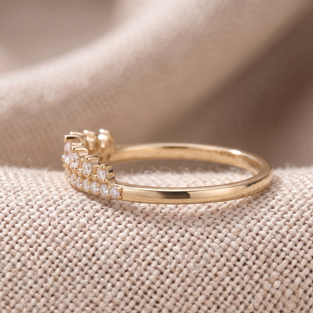 A gold ring with a pavé diamond band and a small diamond accent on the opposite side, resting on a textured beige fabric background.