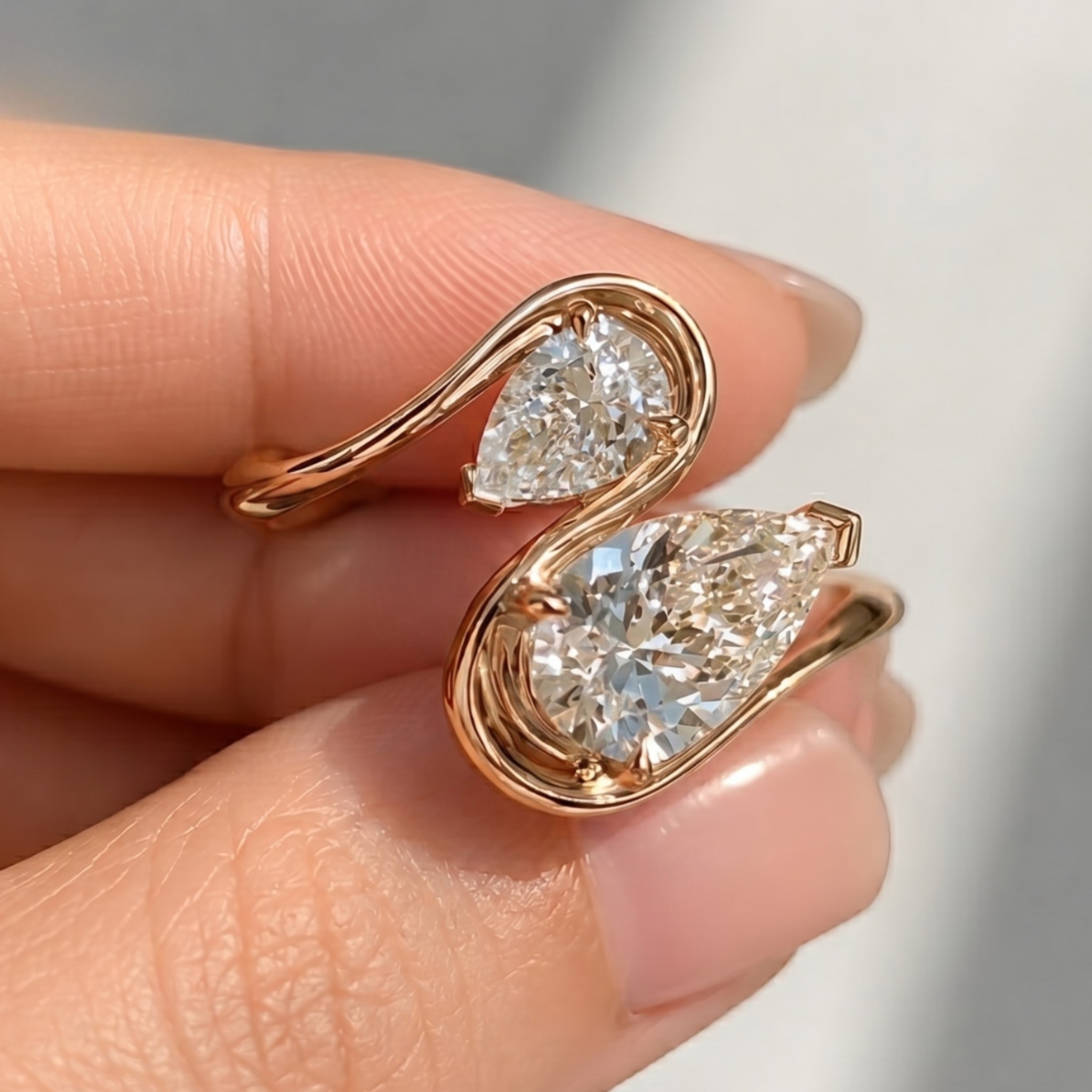 A close-up of a hand holding a gold ring with two pear-cut clear gemstones in a swan-like curved setting.