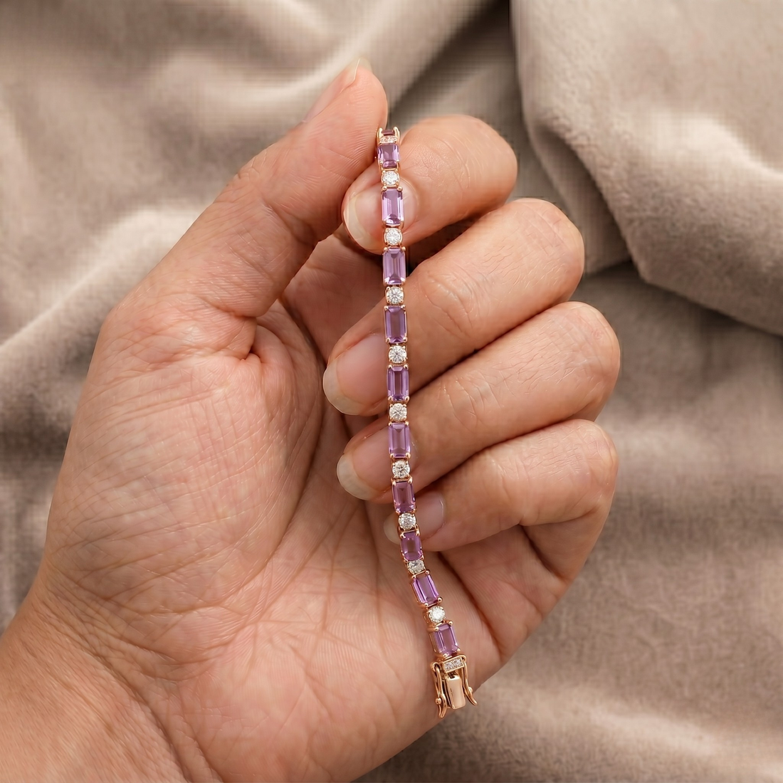 A close-up of a hand holding a delicate tennis bracelet with rectangular purple gemstones and small white stones set in rose gold, against a soft beige fabric background.