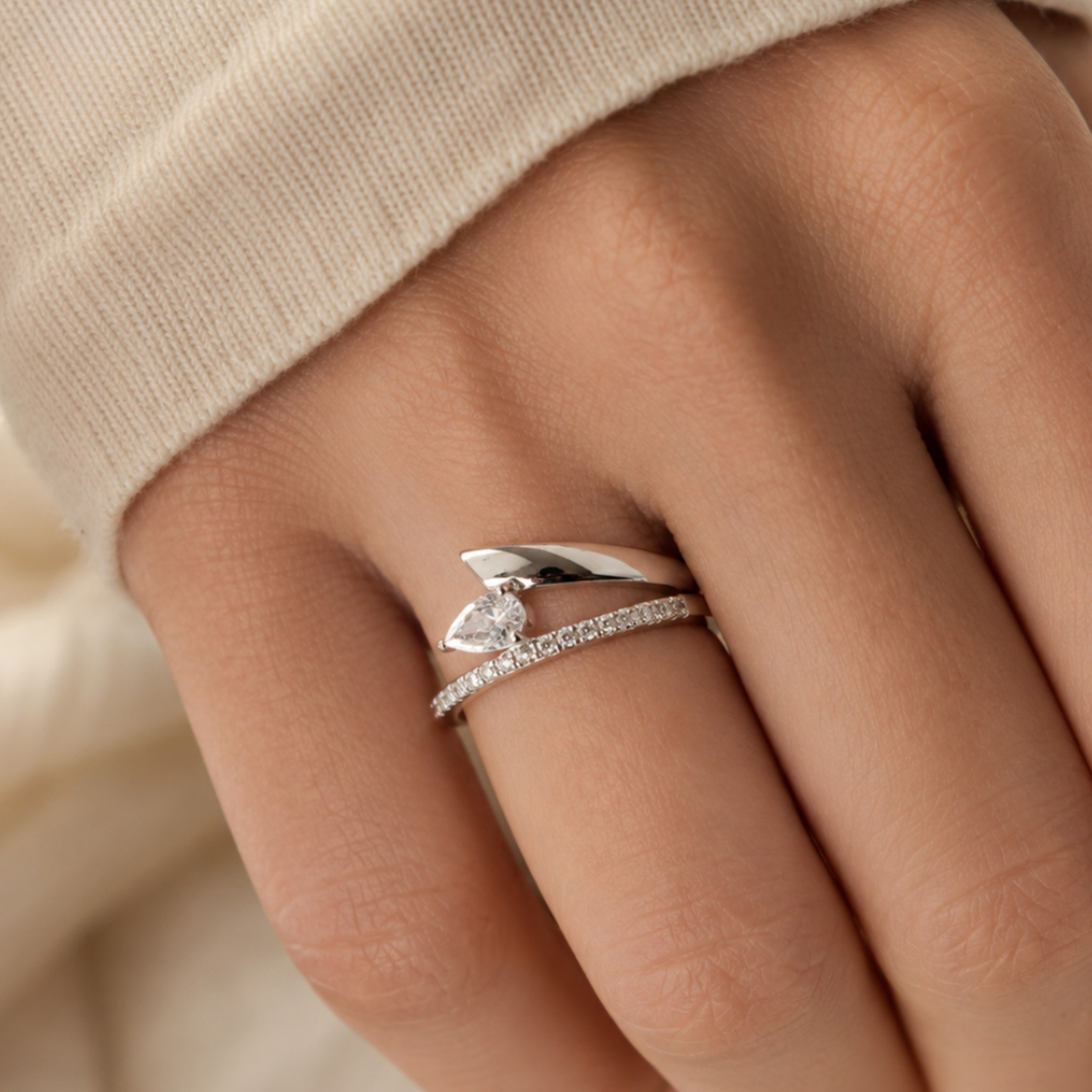 A close-up of a hand wearing a silver ring with a marquise-cut center stone and a pavé band, styled with a beige knit sleeve.