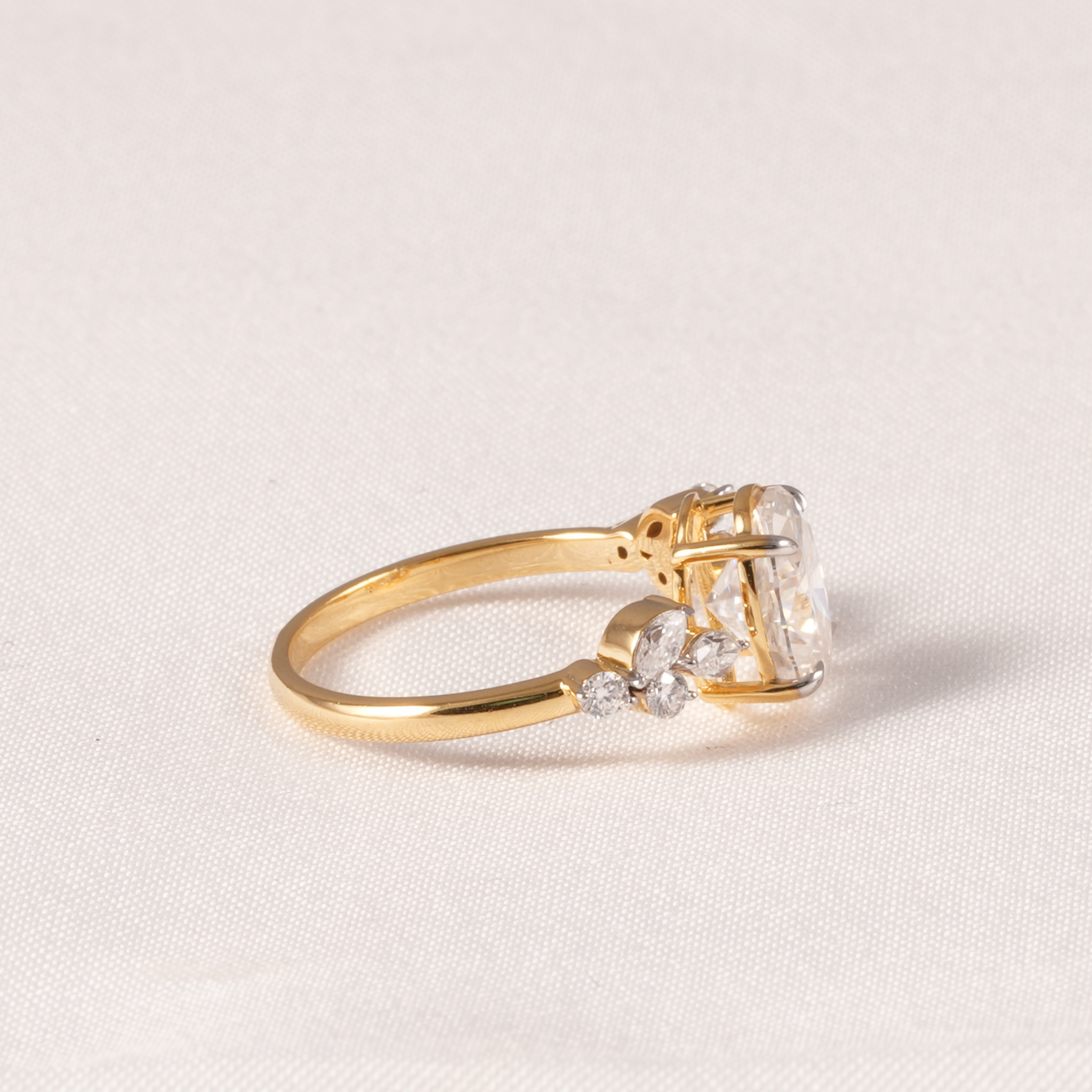 A yellow gold ring with a large clear rectangular gemstone and smaller clear stones on the shoulders, photographed on a light beige fabric background.