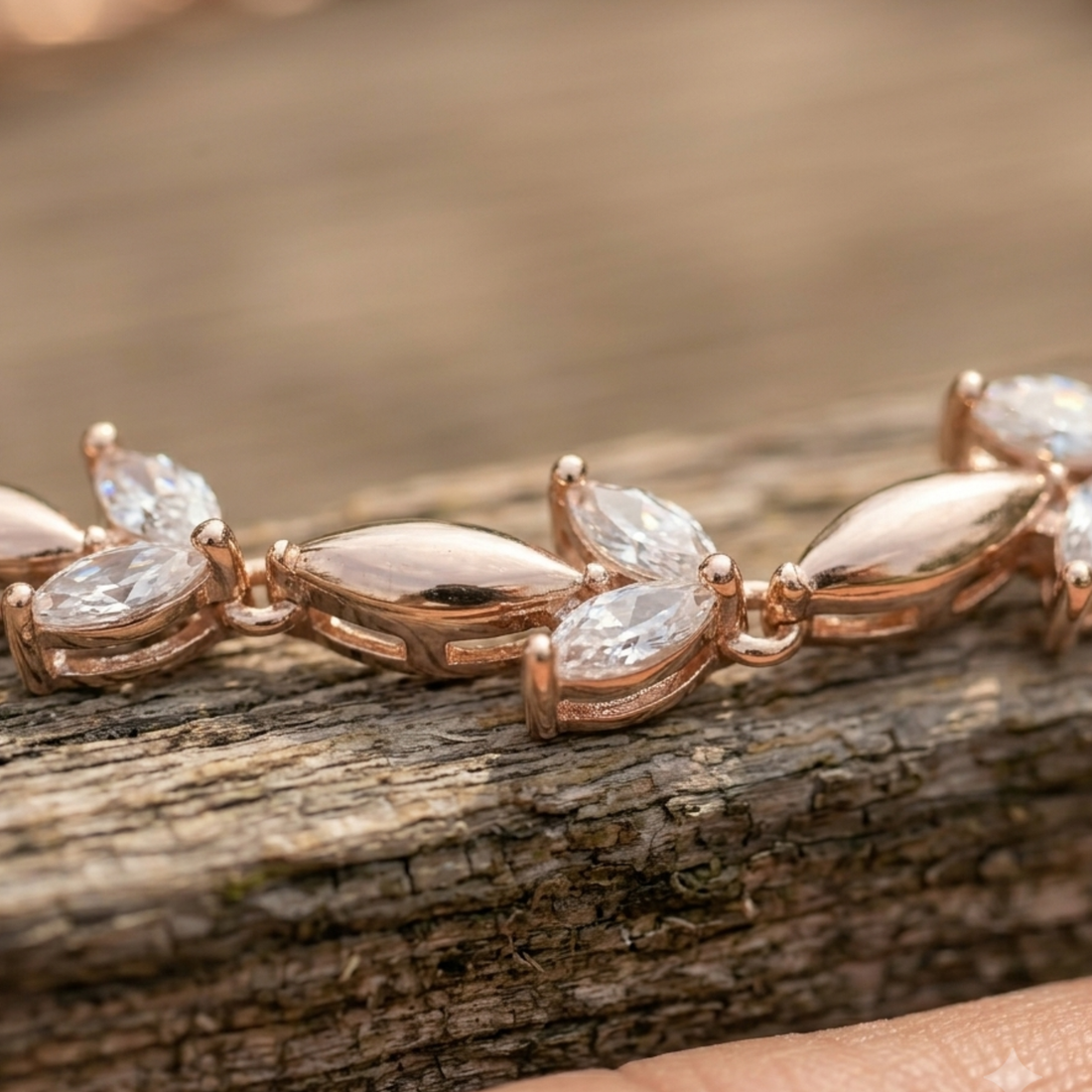 Rose gold jewelry featuring marquise-cut clear gemstones set in a polished metal, shown resting on a textured wooden surface.