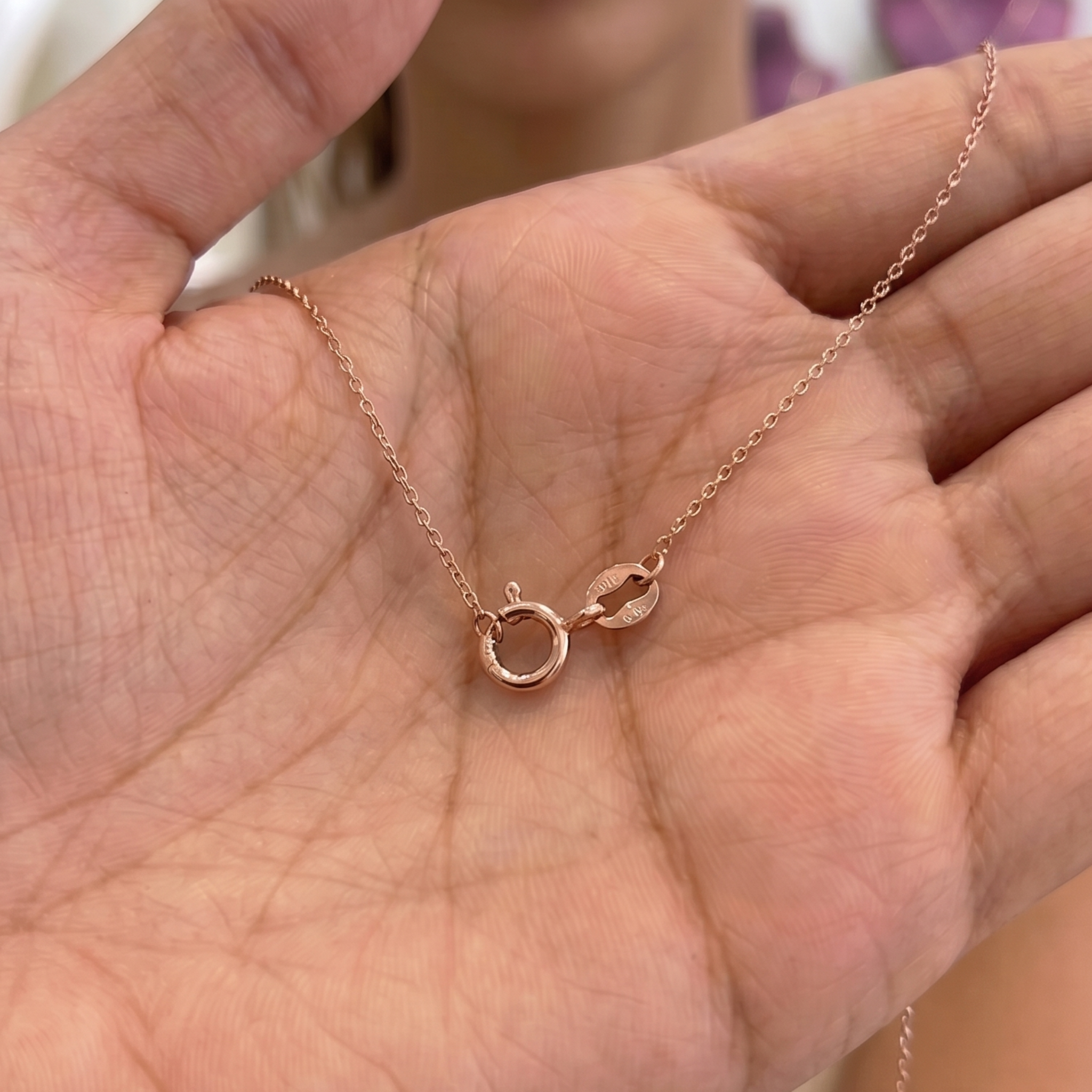 A delicate rose gold necklace with a small circular ring and a tiny crescent moon charm, displayed on an open hand.