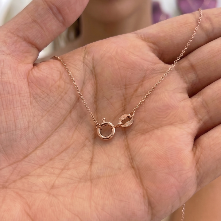 A delicate rose gold necklace with a small circular ring and a tiny crescent moon charm, displayed on an open hand.