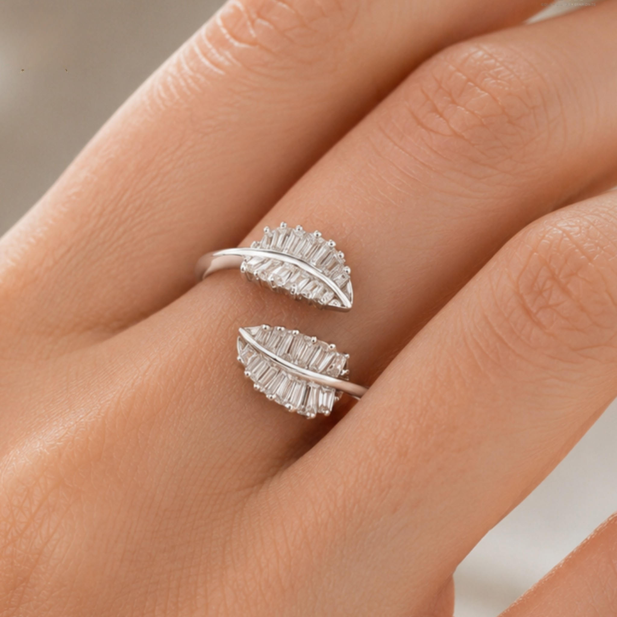 A pair of silver wrap rings designed as leaves, featuring baguette-cut clear stones, shown worn on a person's hand.