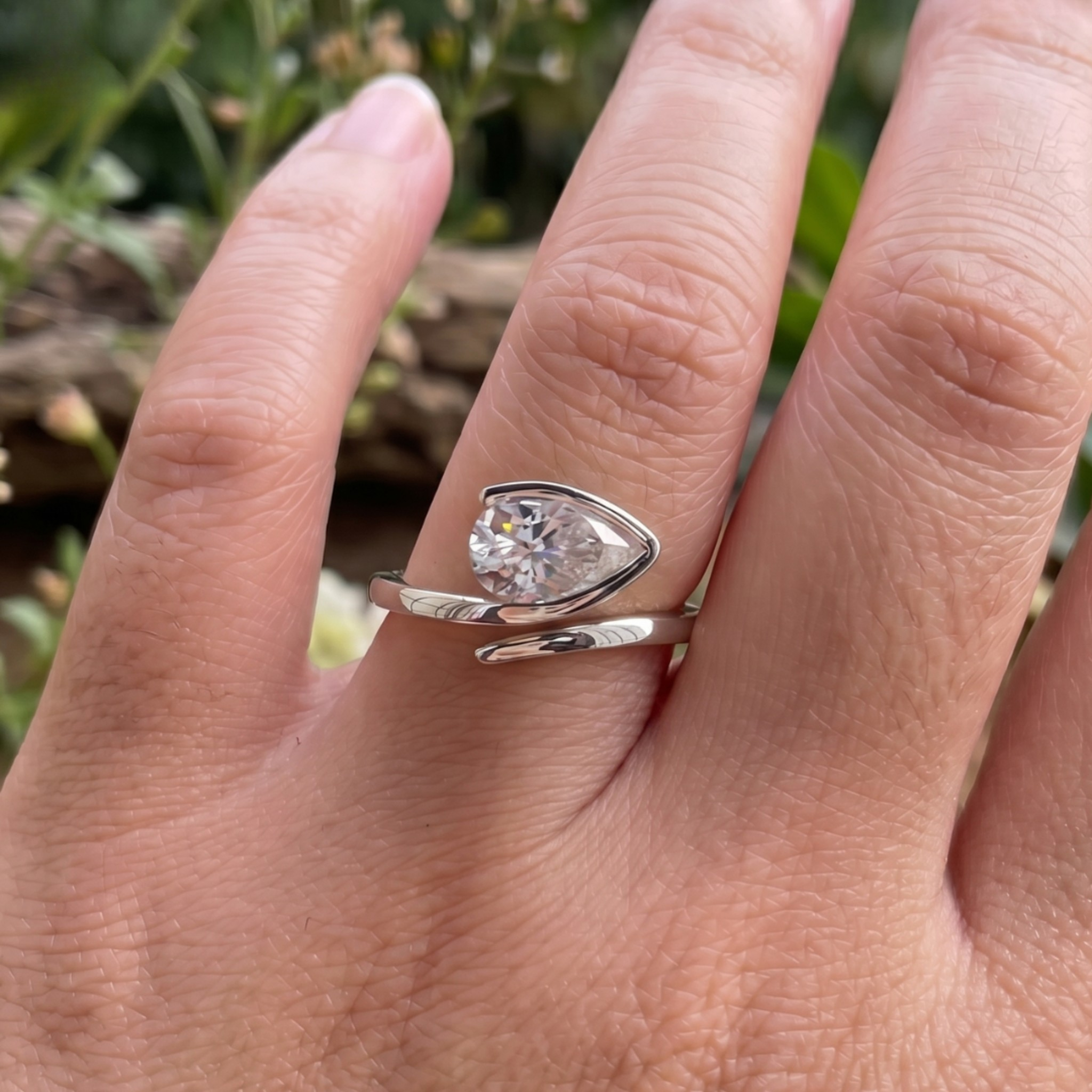 A silver ring with a marquise-cut clear gemstone displayed on a person's finger, with a blurred natural background.