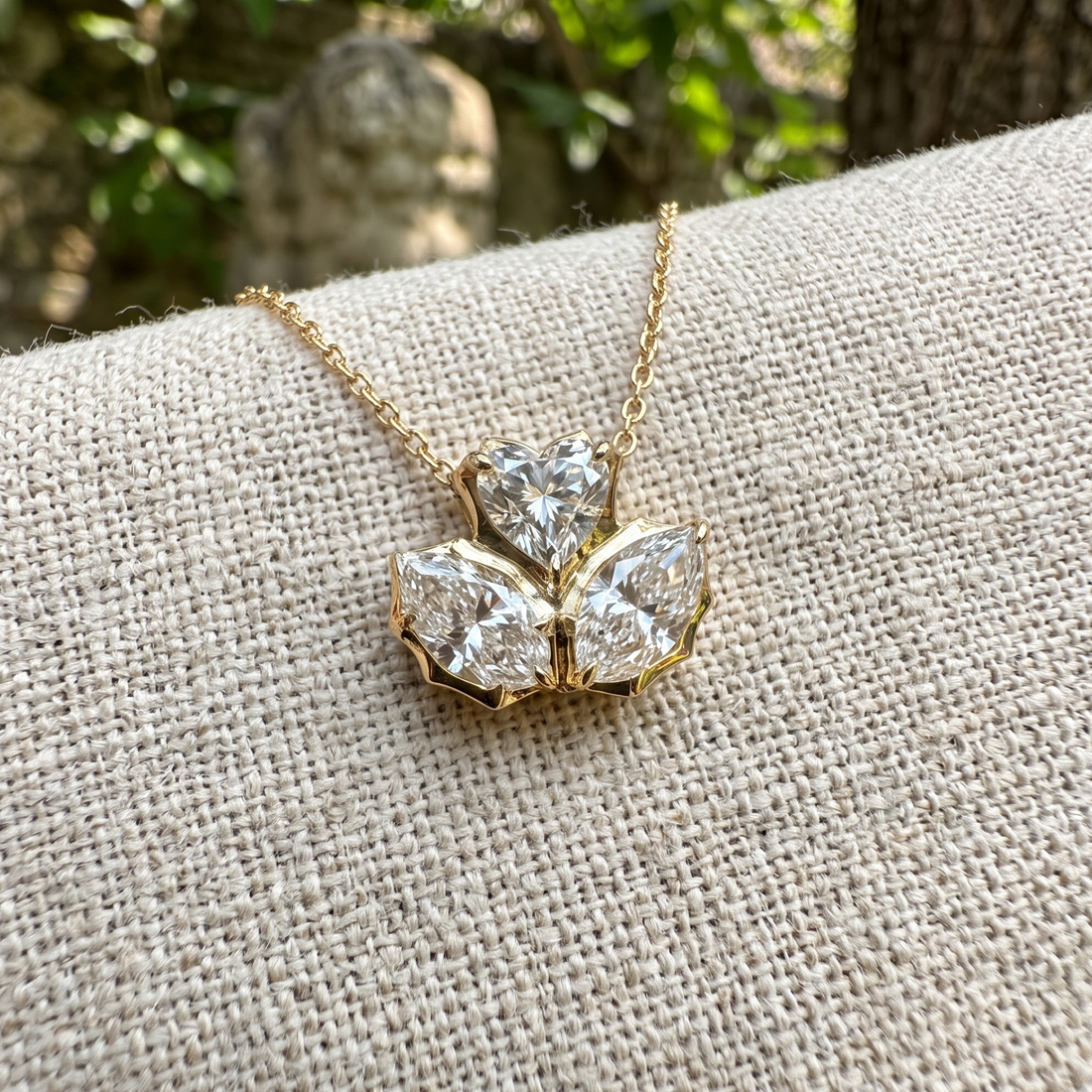 A gold pendant necklace with three clear gemstones arranged in a flower-like cluster
