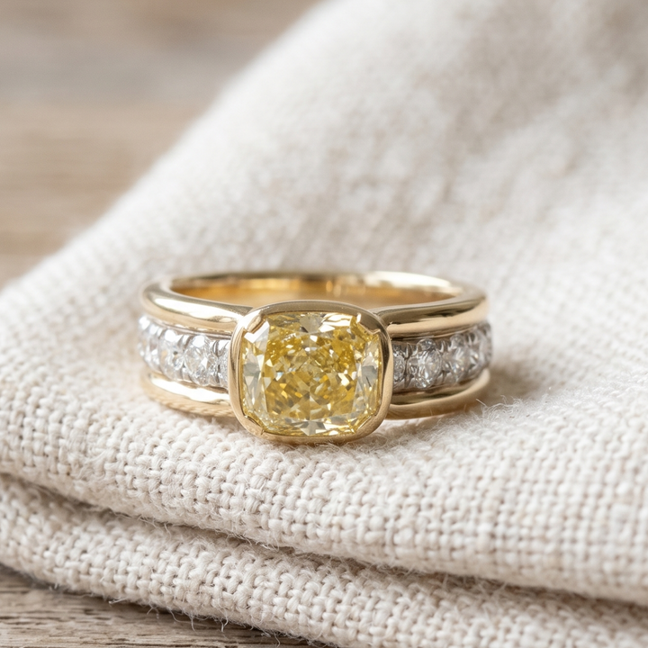 A yellow gold ring featuring a cushion-cut yellow center stone and diamond accents on the band, resting on a textured beige linen fabric.