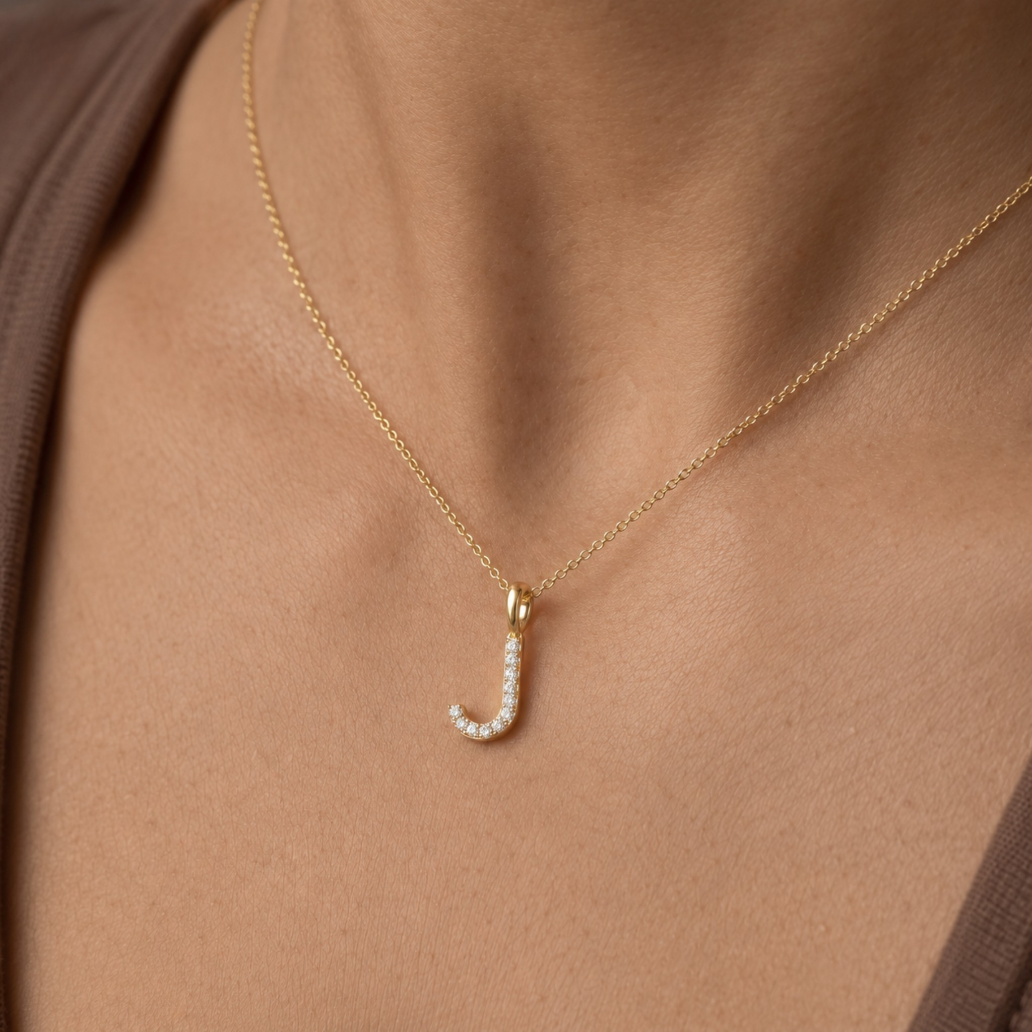 A close-up of a person's neck and chest wearing a delicate gold chain necklace with a small curved pendant set with tiny clear stones.