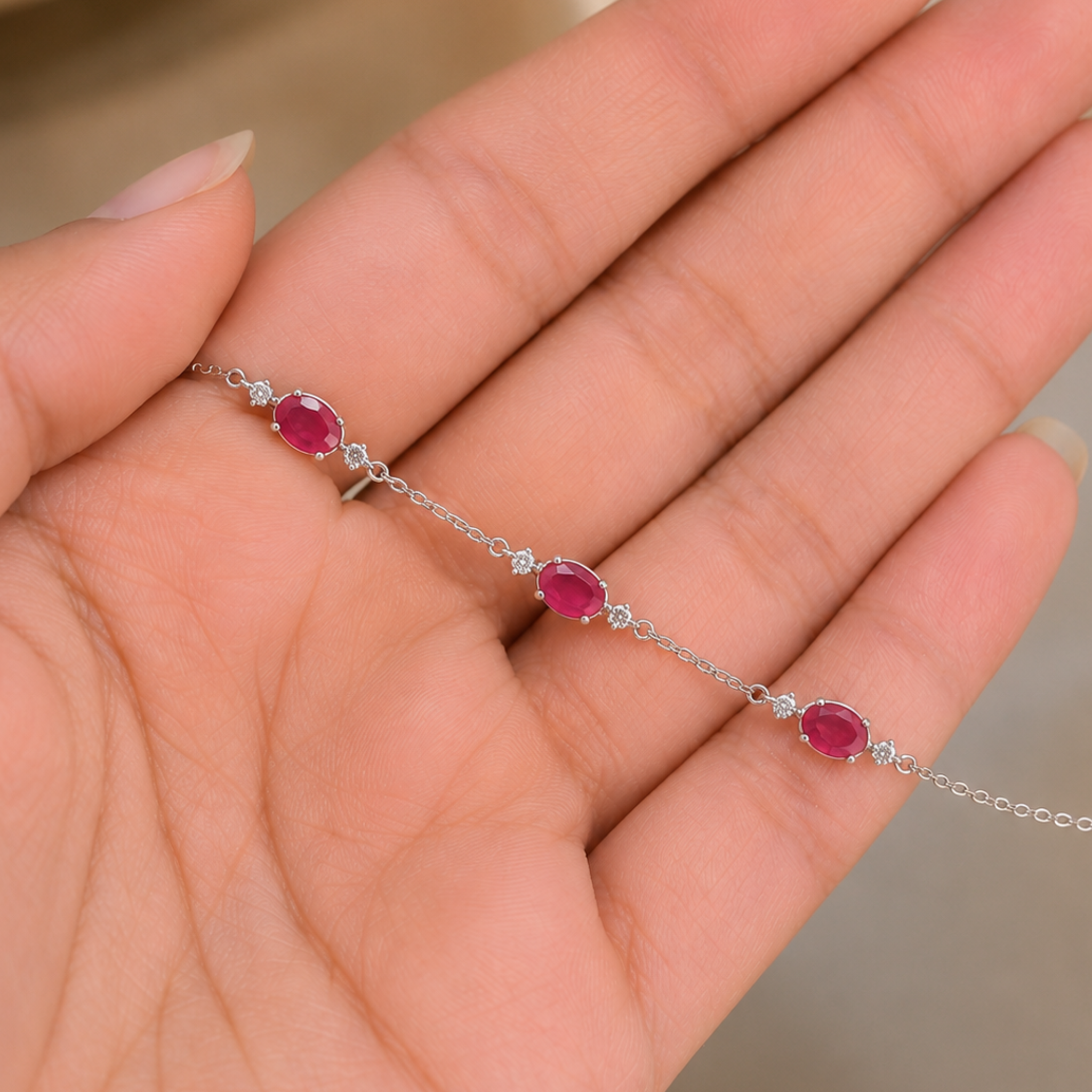 A delicate silver chain bracelet with three oval pinkish-red gemstones and small clear stones, shown resting on an open hand.