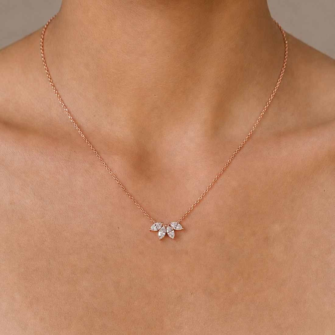 A delicate rose gold chain necklace with a small three-stone leaf cluster pendant, shown worn on a model's neck.