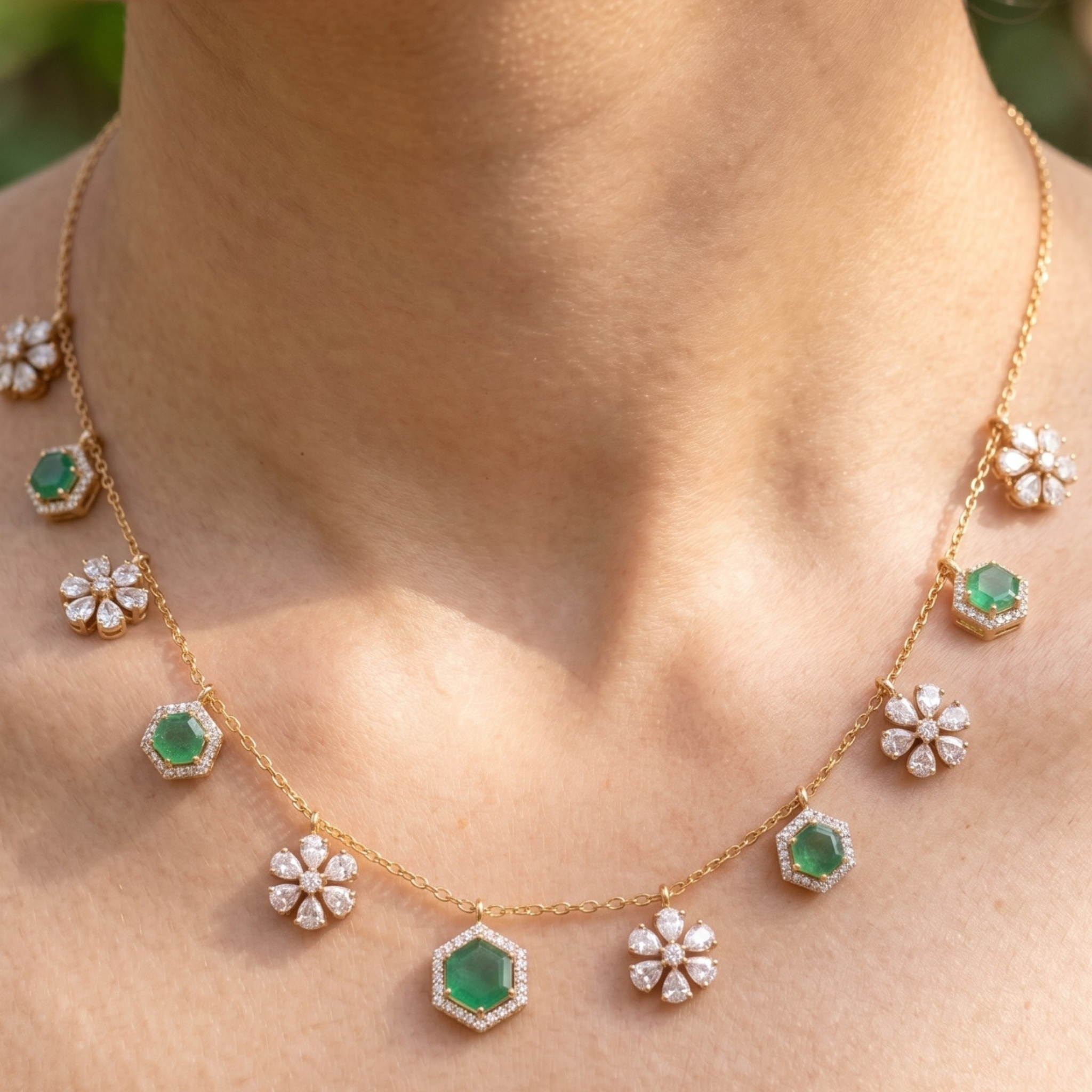 A gold necklace with green emerald-cut stones and white flower-shaped pavé accents, shown worn on a person's neck.