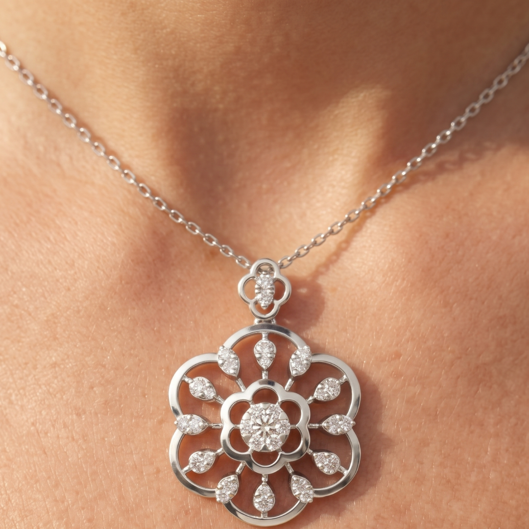 A silver-tone floral pendant necklace with clear gemstones, shown worn on a person's neck against a warm skin-toned background.