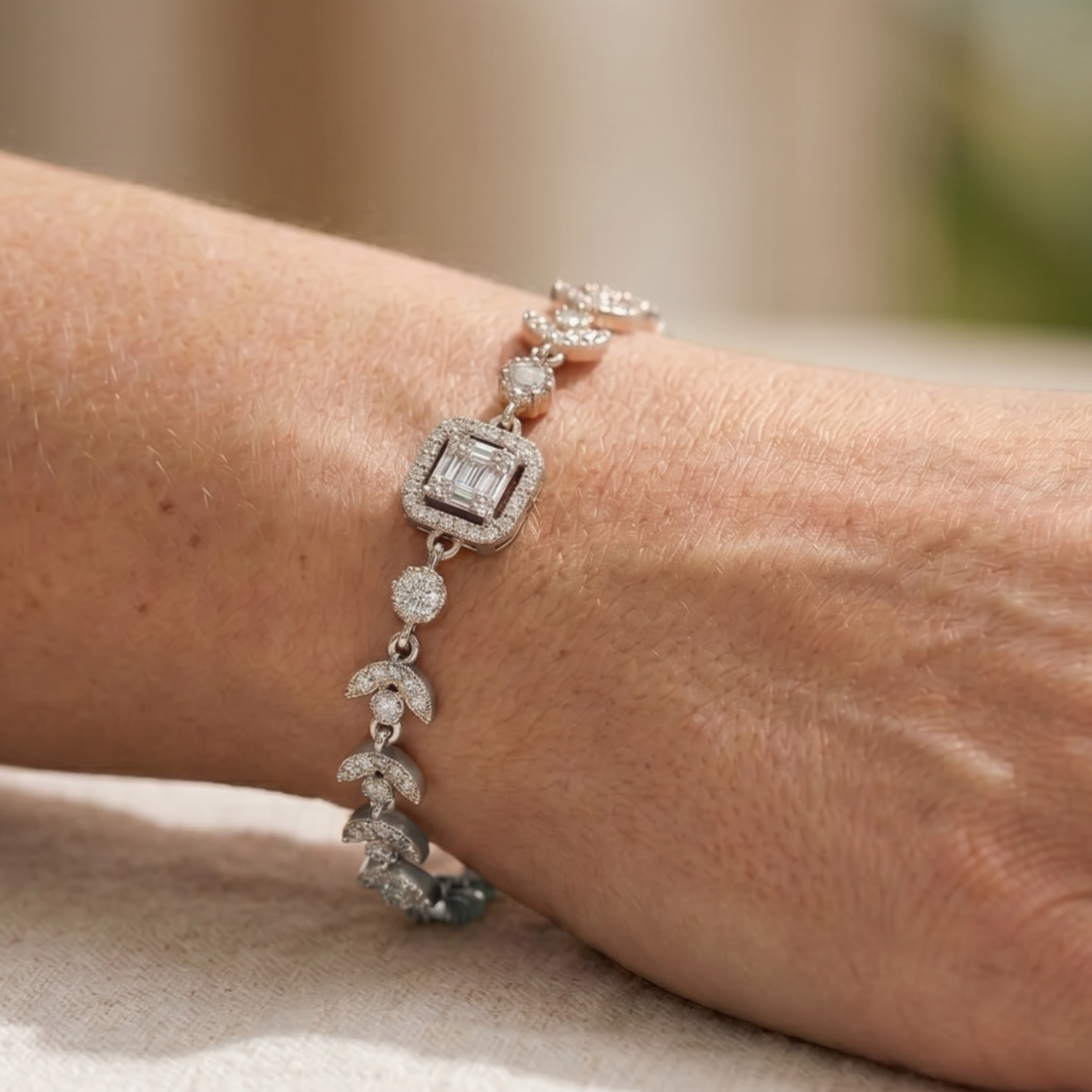 A close-up of a silver-toned bracelet with pavé-set clear stones and a central square baguette gemstone, worn on a person's wrist.